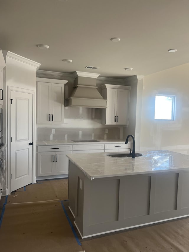 kitchen featuring cooktop, decorative backsplash, an island with sink, custom exhaust hood, and a sink