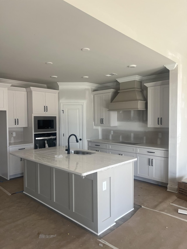 kitchen with stainless steel microwave, a large island with sink, premium range hood, a sink, and black oven