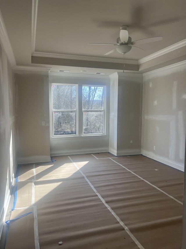 empty room with ceiling fan, baseboards, a raised ceiling, and crown molding