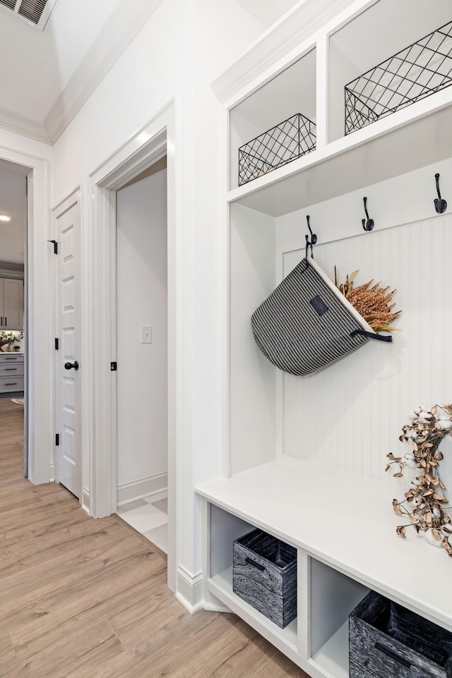 mudroom with baseboards, ornamental molding, visible vents, and light wood-style floors