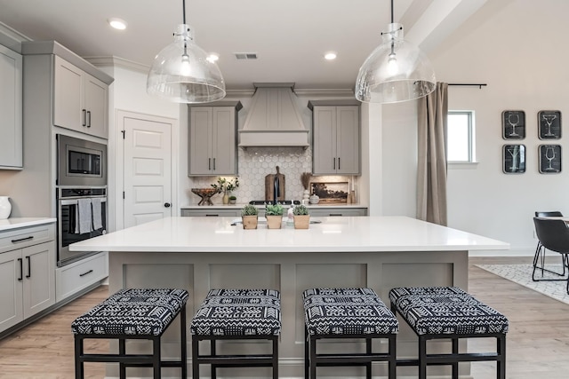 kitchen featuring visible vents, appliances with stainless steel finishes, gray cabinets, a kitchen bar, and custom range hood