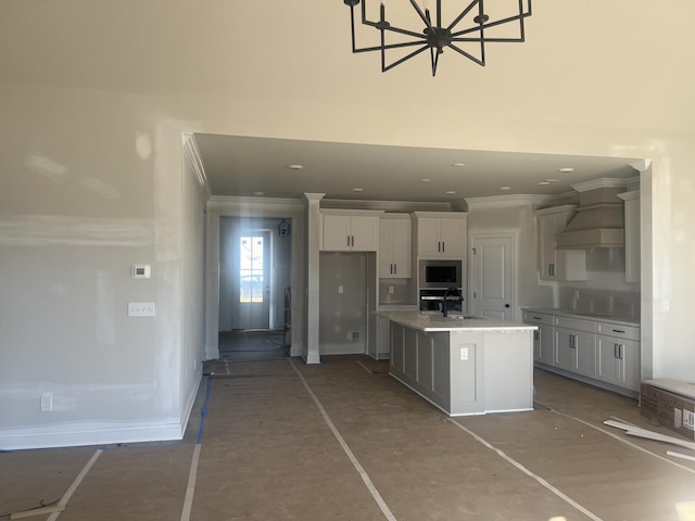 kitchen with wall chimney range hood, a kitchen island with sink, white cabinetry, and crown molding