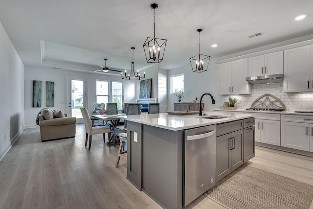 kitchen with under cabinet range hood, stainless steel appliances, a sink, open floor plan, and decorative backsplash