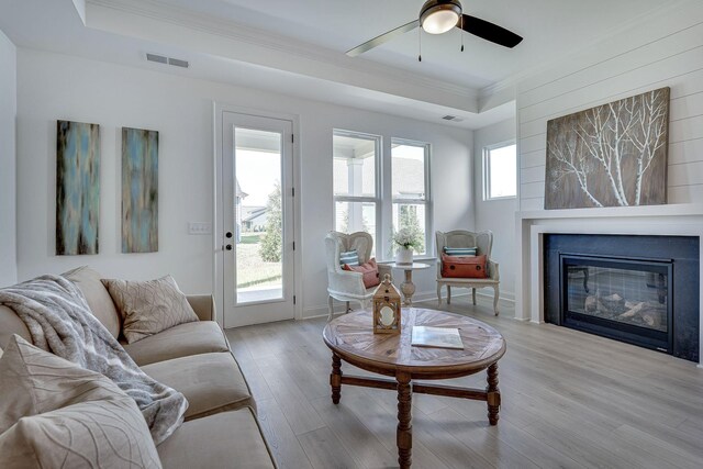 living room with a healthy amount of sunlight, crown molding, visible vents, and light wood finished floors