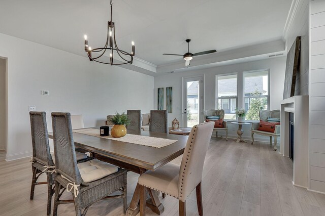 dining area featuring a fireplace, a raised ceiling, ornamental molding, light wood-type flooring, and baseboards