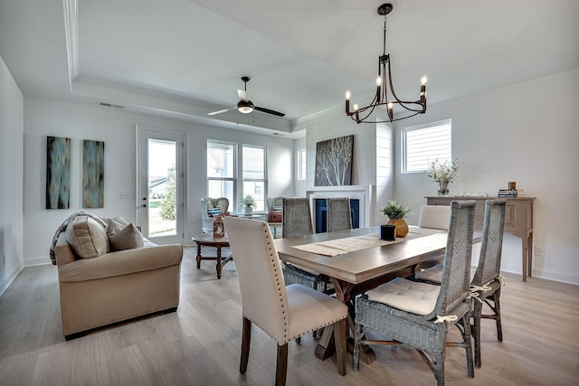 dining space with visible vents, baseboards, a tray ceiling, light wood-style flooring, and ceiling fan with notable chandelier