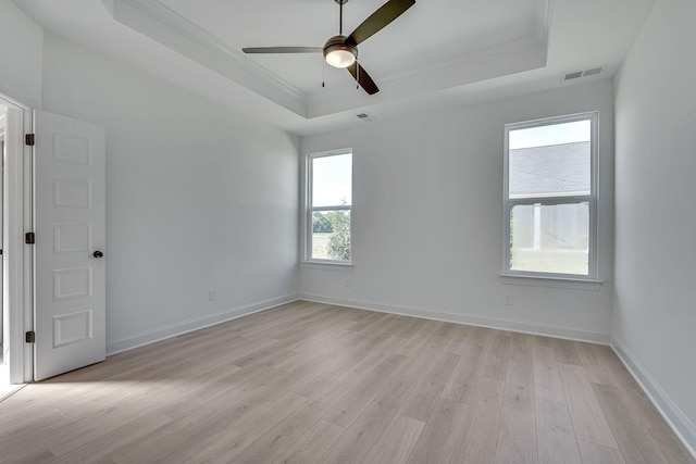 empty room with light wood-style floors, a raised ceiling, ornamental molding, and baseboards