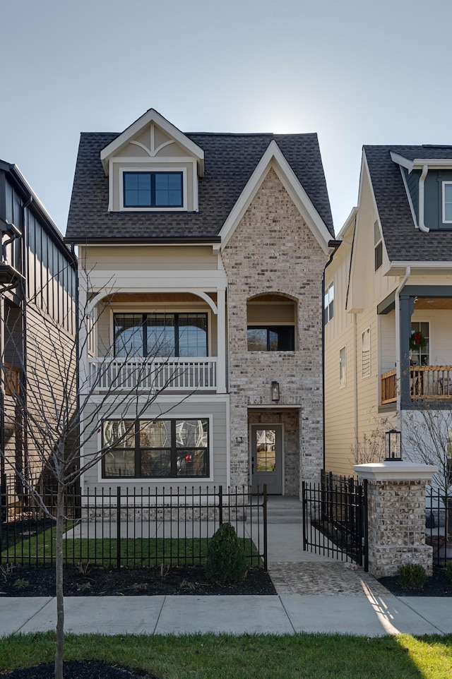 view of front of house featuring a balcony, a fenced front yard, a shingled roof, and brick siding