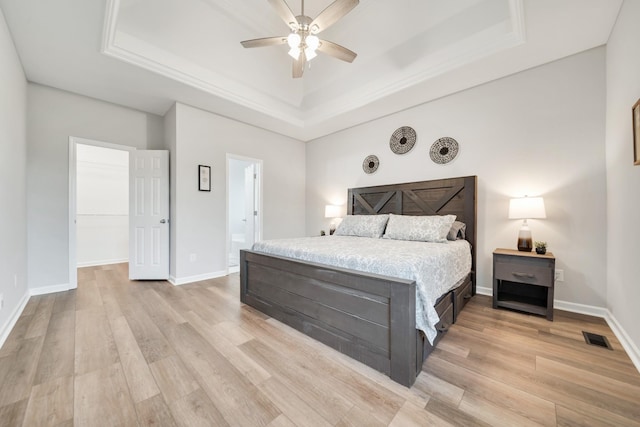 bedroom with baseboards, a tray ceiling, visible vents, and light wood-style floors