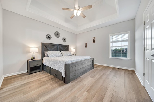 bedroom with light wood-style floors, visible vents, baseboards, and a raised ceiling