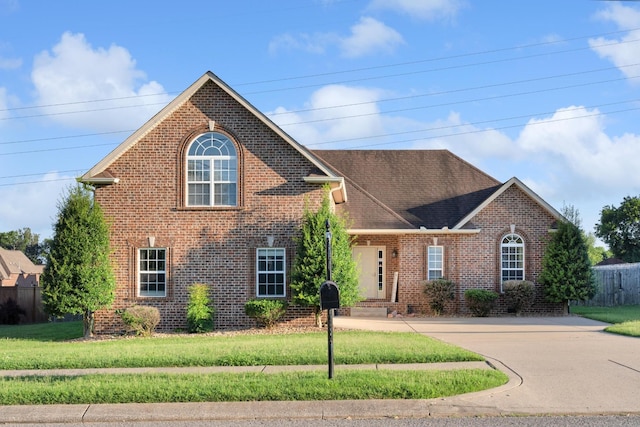 traditional-style house featuring roof with shingles, a front yard, and brick siding