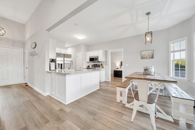 kitchen with appliances with stainless steel finishes, white cabinets, a peninsula, and light wood finished floors