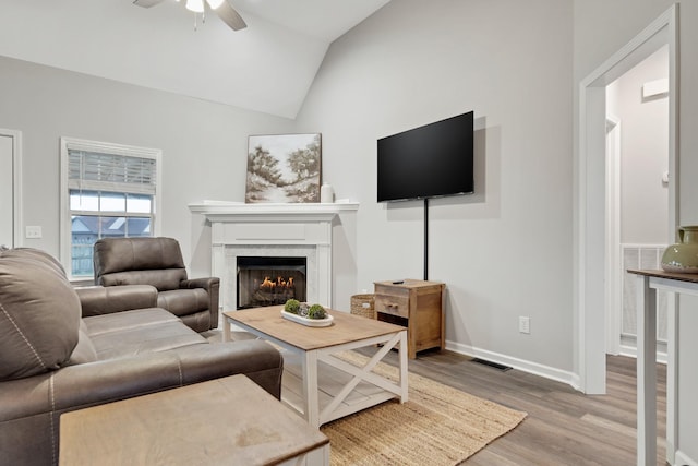 living room featuring visible vents, baseboards, a ceiling fan, light wood-style flooring, and vaulted ceiling