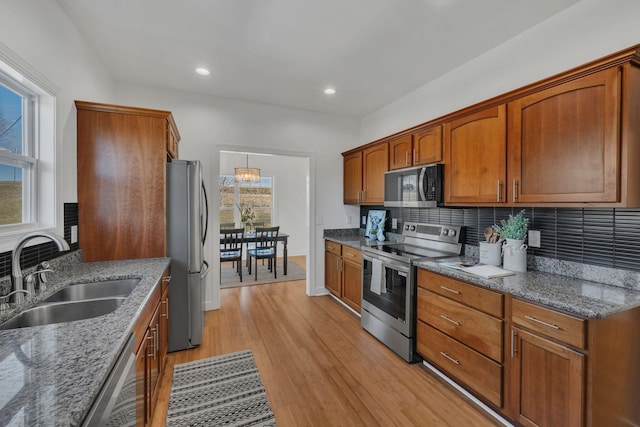 kitchen with brown cabinets, backsplash, appliances with stainless steel finishes, light wood-style floors, and a sink