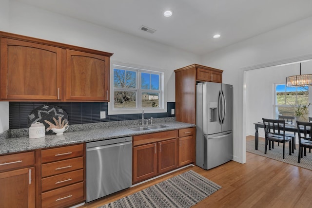 kitchen with brown cabinetry, decorative backsplash, light wood-style flooring, stainless steel appliances, and a sink