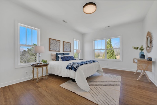 bedroom with baseboards, visible vents, and wood finished floors