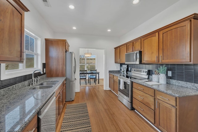 kitchen featuring appliances with stainless steel finishes, light wood-type flooring, a sink, and brown cabinets