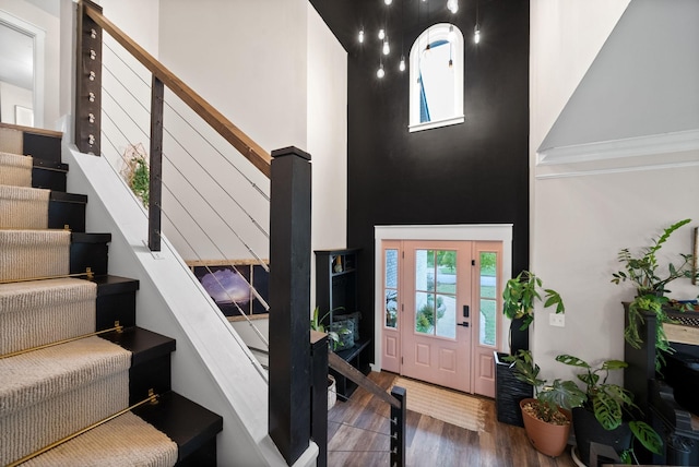 foyer entrance with stairway, a towering ceiling, and wood finished floors