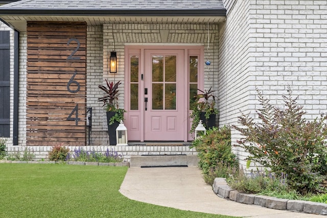 entrance to property with a yard, brick siding, and a shingled roof