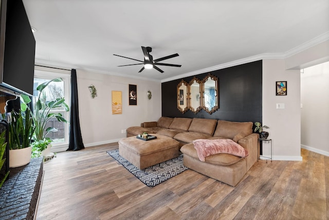 living area featuring a ceiling fan, crown molding, baseboards, and wood finished floors