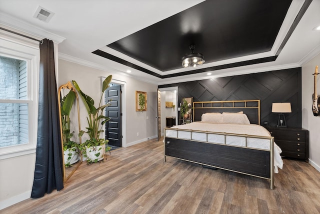 bedroom featuring visible vents, crown molding, a tray ceiling, and wood finished floors