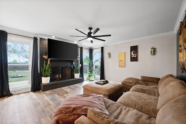 living area featuring light wood finished floors, ornamental molding, a brick fireplace, and a ceiling fan