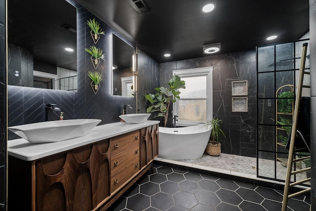 full bathroom with a freestanding tub, a sink, visible vents, and tile walls