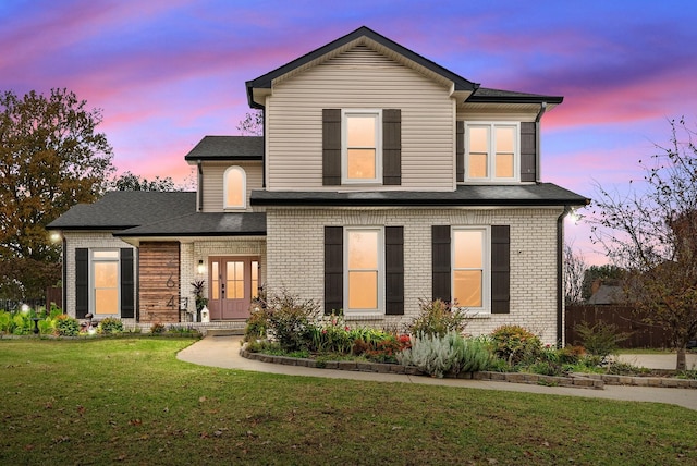 traditional-style house featuring a shingled roof, a front lawn, french doors, and brick siding