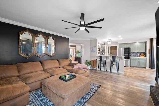 living room featuring baseboards, light wood-type flooring, a ceiling fan, and crown molding