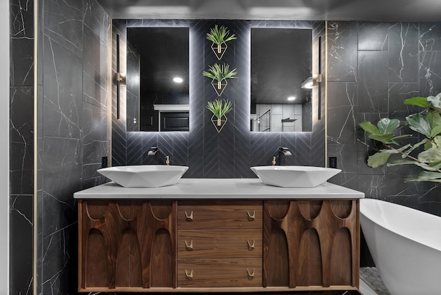 bathroom with a freestanding bath, double vanity, a sink, and tile walls