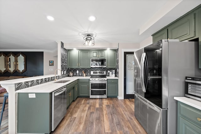 kitchen with stainless steel appliances, light countertops, a sink, green cabinetry, and a peninsula