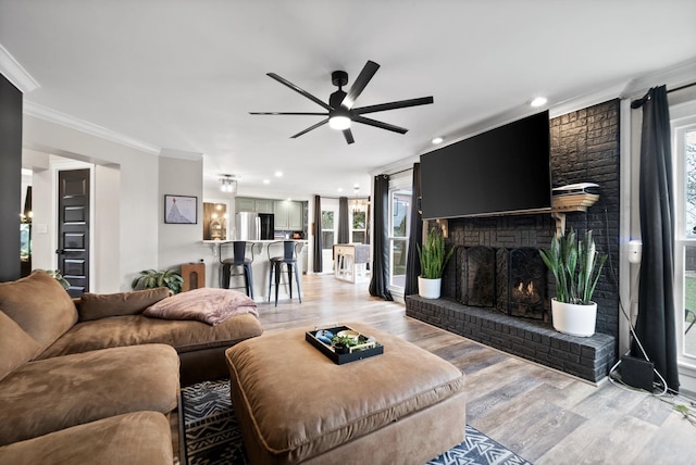 living room with light wood finished floors, a fireplace, ornamental molding, and a wealth of natural light