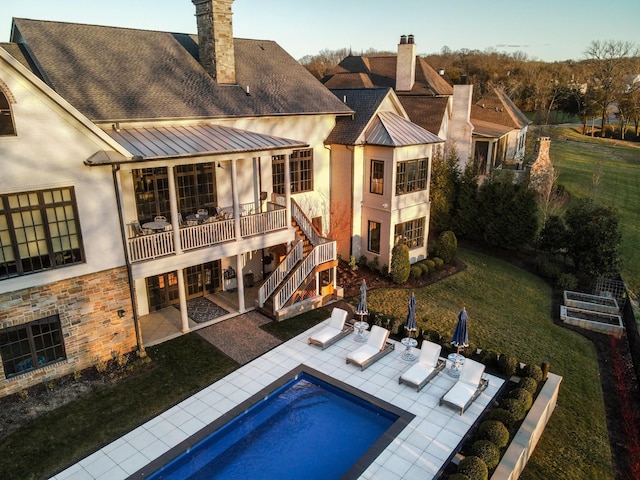 rear view of property featuring a standing seam roof, a patio area, and a chimney