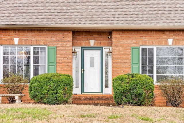 doorway to property with brick siding and a shingled roof