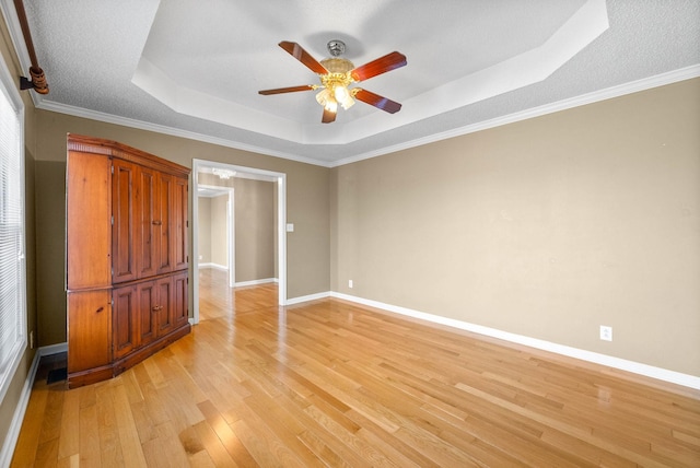 unfurnished bedroom with a raised ceiling, crown molding, light wood-style floors, and baseboards