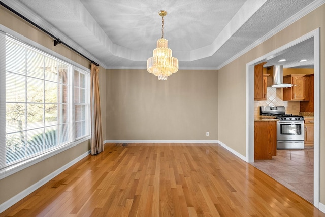 unfurnished dining area with a raised ceiling, baseboards, light wood finished floors, and a chandelier