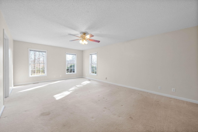 unfurnished room featuring light carpet, ceiling fan, a textured ceiling, and baseboards