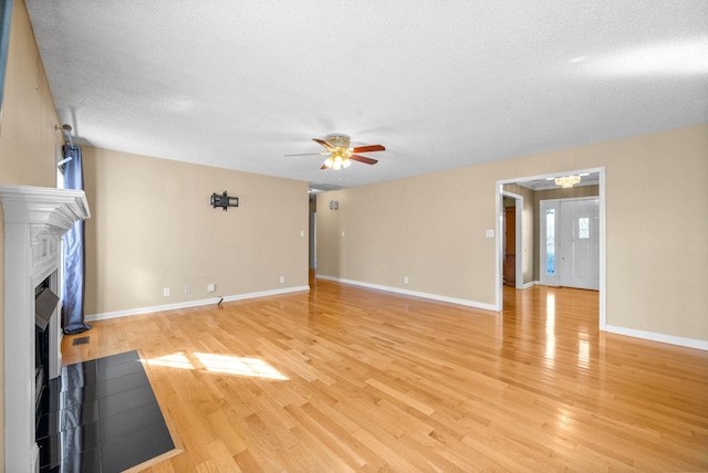 unfurnished living room with baseboards, a fireplace with flush hearth, a textured ceiling, ceiling fan with notable chandelier, and light wood-type flooring