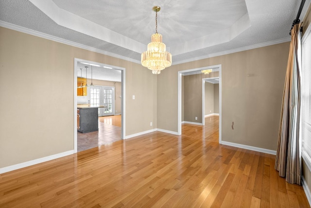 unfurnished room with a notable chandelier, baseboards, a raised ceiling, and light wood-style floors