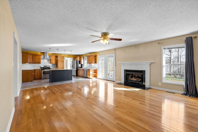 unfurnished living room with visible vents, light wood-style flooring, plenty of natural light, and a fireplace with flush hearth