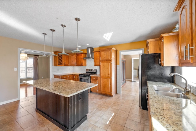 kitchen with a sink, a kitchen island, appliances with stainless steel finishes, wall chimney range hood, and decorative backsplash