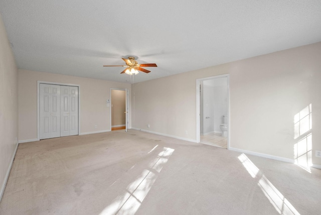 unfurnished bedroom with a ceiling fan, ensuite bath, a closet, baseboards, and light colored carpet