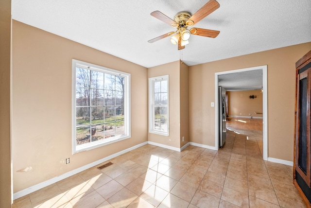 spare room with light tile patterned floors, a ceiling fan, baseboards, visible vents, and a textured ceiling