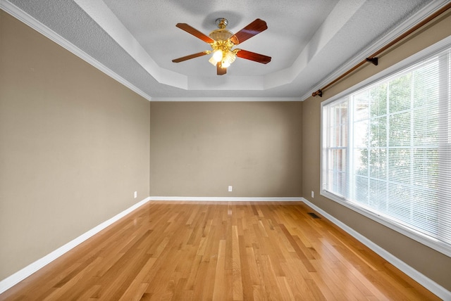 spare room with baseboards, a raised ceiling, light wood-style floors, and visible vents