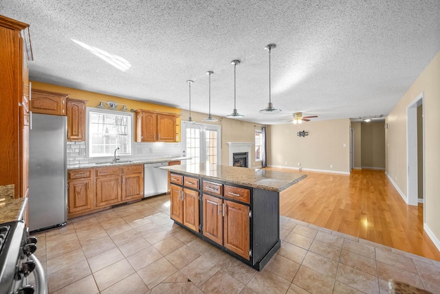 kitchen with a center island, decorative backsplash, a fireplace, hanging light fixtures, and stainless steel appliances