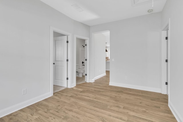 unfurnished room with baseboards, attic access, and light wood-style floors