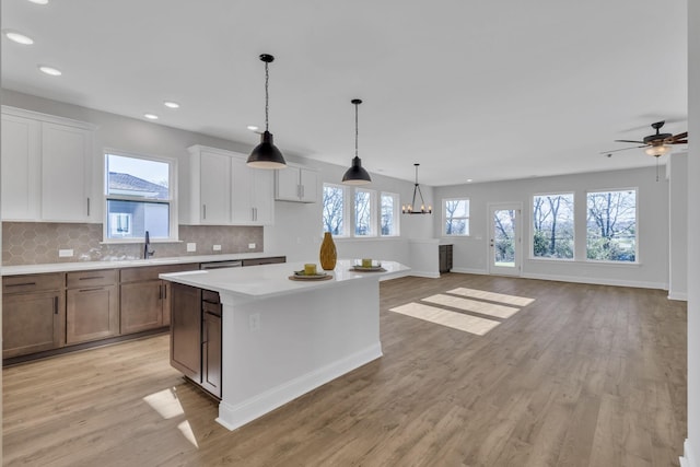 kitchen with a center island, light countertops, light wood-style flooring, backsplash, and white cabinetry