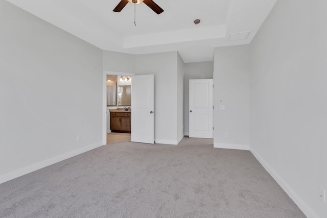 unfurnished bedroom featuring ceiling fan, light colored carpet, baseboards, a tray ceiling, and ensuite bath