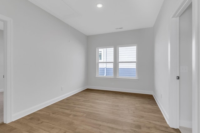 unfurnished room featuring light wood-type flooring, attic access, visible vents, and baseboards