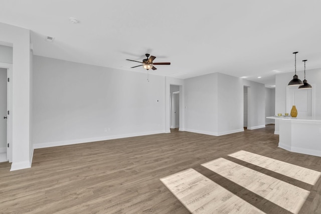 unfurnished living room with a ceiling fan, baseboards, and wood finished floors